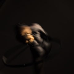 Performer Chiara Paradisi in posa su cerchio aereo (aerial hoop) con body painting nero su fondo nero - Fotografia di Alessandro Tintori