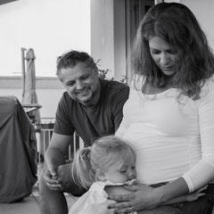 Familien Fotoshooting in Offenbach. Die Tochter kukschelt den schwangeren Bauch der Mutter. 