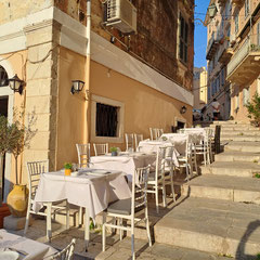 Griechisches Restaurant mit weißgedeckten Tischen. Pastellfarbene venezianische Bauten in der Altstadt von Korfu-Stadt