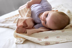 Baby mit lilafarbenen Body auf Mulltüchern von LÄSSIG