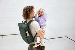 Papa mit Wickelrucksack und Baby auf dem Arm