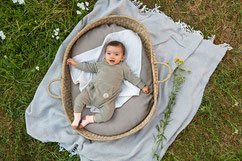 Baby mit Frotteeoverall im Babykorb auf der Wiese
