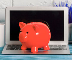 Laptop vor einer weißen Wand mit einem roten Sparschwein