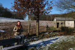 Winterlandschap met op de helling een bos en op de voorgrond een vrouw zittend op een bank. Een beschutting voor vee op de rechterkant.