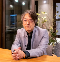 平賀敬一郎建築研究所の代表・建築家、平賀敬一郎のプロフィール写真。柔らかな光に包まれた洗練された空間で、リラックスした表情でこちらを見つめる思索のポートレート。