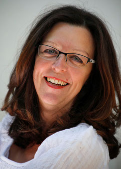 Porträtfoto von Sybille mit weißer Bluse. Sybille schaut strahlend ins Bild.