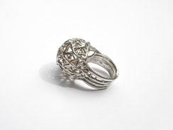 Bague boule en argent très ajourée posée de profil sur fond blanc.