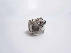 Une bague en argent avec une pierre transparente est posée sur un fond blanc.