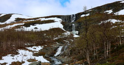 Sehenswürdigkeiten Kilpisjärvi: Ein malerischer Wasserfall fällt entlang von Schneefelder in die Tiefe.