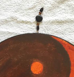 Detail Oceandrum Yin en Yang in donkerbruine en warmoranje aquarelverf. Het ophangsysteem heeft donkerbruine en kleine oranje kralen aan kettingdraad met lusje