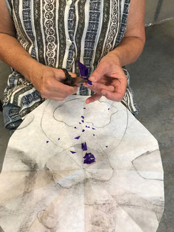 Een vrouw met een zwartwitteblouse aan, is het een schaartje stukje weg aan het knippen uit een vierdubbel gevouwen stuk paars vloeipapier