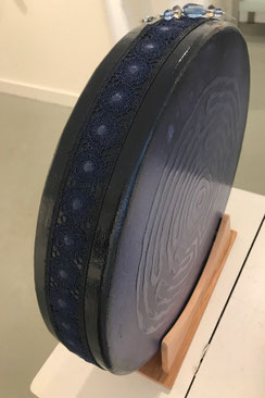 Metallic lichtblauwe oceandrum, met daarop een doorzichtige dikke laag in de vorm van Labyrint. Aan de zijkant een dionkerblauwe laklaag met bijpassend lint en ophanger. Schilderij en muziekinstrument in één.