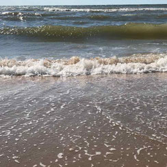 Opkomend tij, met grote groen grijze gloven, en op het natte strand de schuimbelletjes als het water terugloopt naar zee