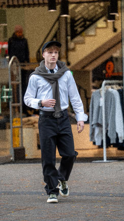 Junger Mann in Einkaufszentrum, bekleidet mit schwarzer Levis-Jeans, helles Hemd und grauem Pullover.