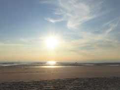 brauner Strand vor untergehender Sonne, die sich im Wasser spiegelt 