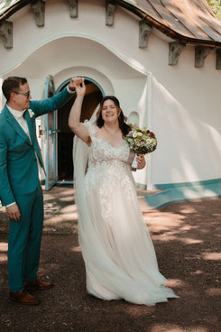 Bräutigam dreht lachende Braut vor weißer Kapelle beim Brautpaar-Shooting, Hochzeitsfotografie Herxheim Südpfalz