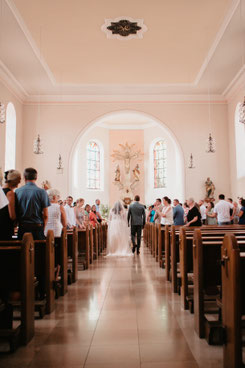 Brautpaar zieht gemeinsam durch die Dorfkirche Herxheim-Hayna beim Einzug zur kirchlichen Trauung, Hochzeitsfotografie Pfalz