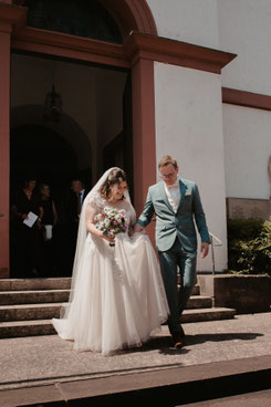 Brautpaar verlässt Hand in Hand die Kirche Herxheim-Hayna nach kirchlicher Trauung, Hochzeitsfotografie Südpfalz
