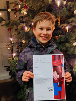 Paul-Jonathan mit der Spendenurkunde am Weihnachtsbaum in der Vöhler Martinskirche.