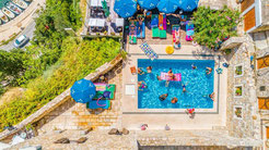 Aerial view of a swimming pool with families enjoying water activities, surrounded by sun loungers and greenery