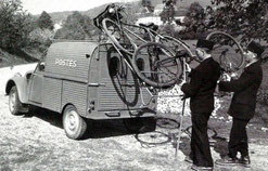 Deux facteurs posant des vélos sur le toit d'une 2CV fourgon des postes