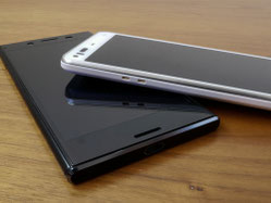 木製テーブルの上に、黒と白のAndroidスマートフォンが重ねて置かれている様子。上の白い端末が下の黒い端末に斜めに重なり、側面のボタンやスピーカー部分が見えるシンプルな構図。