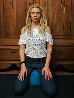 Haltungen zum Mediteren: Der Fersensitz, erhöht auf einem Meditationskissen.