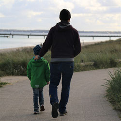 Vater, der mit Sohn am Meer spaziert, liebevoll das Kind begleitend