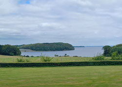 Holsteinische Landschaft: im Vordergrund ein Getreidefeld, im Hintergrund ein See und Wald