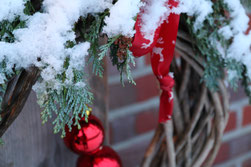 Adventskranz aus Weiden geflochten mit roter Schleife, roten Kugeln und Schnee