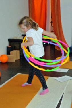Ein Mädchen stellt im Kinderyoga mit mehreren Hula Reifen das schlüpfen aus dem Ei nach