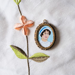Hand-painted portrait medaillon of Jane Austen in antique frame, laying on silk fabric.