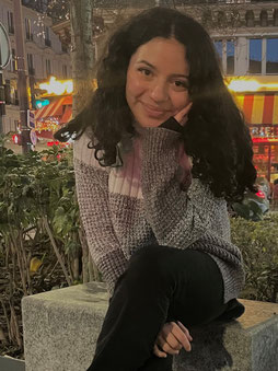 Sara Cabrera Ramirez Portrait - sie sitzt auf einem Stein und lächelt in die Kamera. 