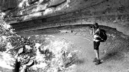 Foto in bianco e nero che mostra Delphicaphoto mentre fotografa il paesaggio all'interno di una cavità naturale