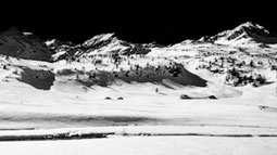 Black and white landscape photograph with snow-capped mountains on a bright day