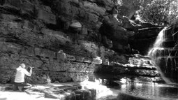 Black and white photo with Delphicaphoto on the left photographing a waterfall on the right