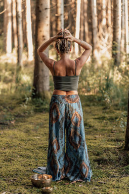 Eine Frau auf dem Boden liegend in der Natur. Ihr Kopf liegt im Schoß einer zweiten Frau, diese Sitzt und hält behütend eine Hand am Rücken und die Andere am Kopf der Liegenden.