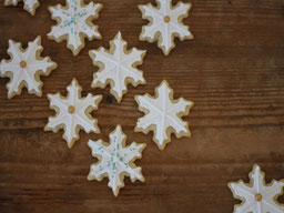 mehrere Kekse in Schneeflockenform mit Royal Icing auf einer Holuplatte