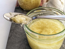 auf einem Holzbrett steht ein Glas Knoblauch Grundstock, ein Löffel liegt quer über dem Glas