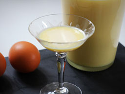 ein Glas Eierlikör, rechts im Hintergrund eine Flasche Eierlikör, links 2 braune Eier