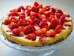 ein Cheesecake mit Brownieboden und frischen Erdbeeren auf einer GlasPlatte