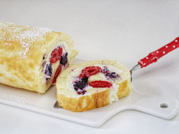 eine Biscuitrolle mit Beeren auf einer weißen Porzellanplatte, eine Scheibe liegt auf einem Kuchenheber mit rotem Griff