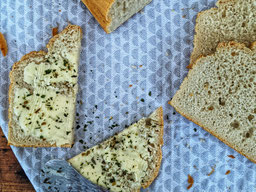 mehrere Scheiben Dinkelvollkornbrot, 2 davon mit Butter bestrichen, auf einem hellgrau gemustertem Küchenhandtuch