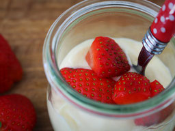 Erdbeer Quark im Glas, frische Erdbeeren liegen auf dem Quark, ein kleiner Löffel mit rotem Griff, steckt seitlich im Glas