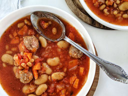 ein Suppenteller mit französischer Bohneneintopf, in der Suppe liegt ein verschnörkelter Suppenlöffel