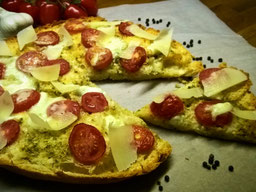 auf einem Backpapier liegt eine FladenbrotPizza, eine Stück ist angeschnitten