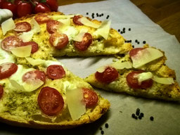 auf einem Backpapier liegt eine FladenbrotPizza, ein Stück ist angeschnitten