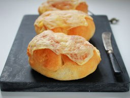 3 Käsebrötchen auf einem dunkelgrauem Marmorbrett, rechts ein Messer