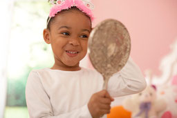 Photo of a little girl admiring her princess tiara in a silver mirror