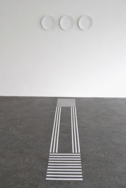 an installation of three white-painted plates on a wall and a guide pattern for the blind on the floor